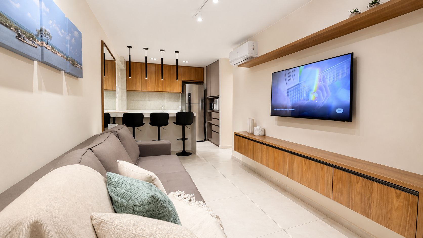 A modern living room with a sofa, a TV mounted on the wall, and a kitchen area in the background.