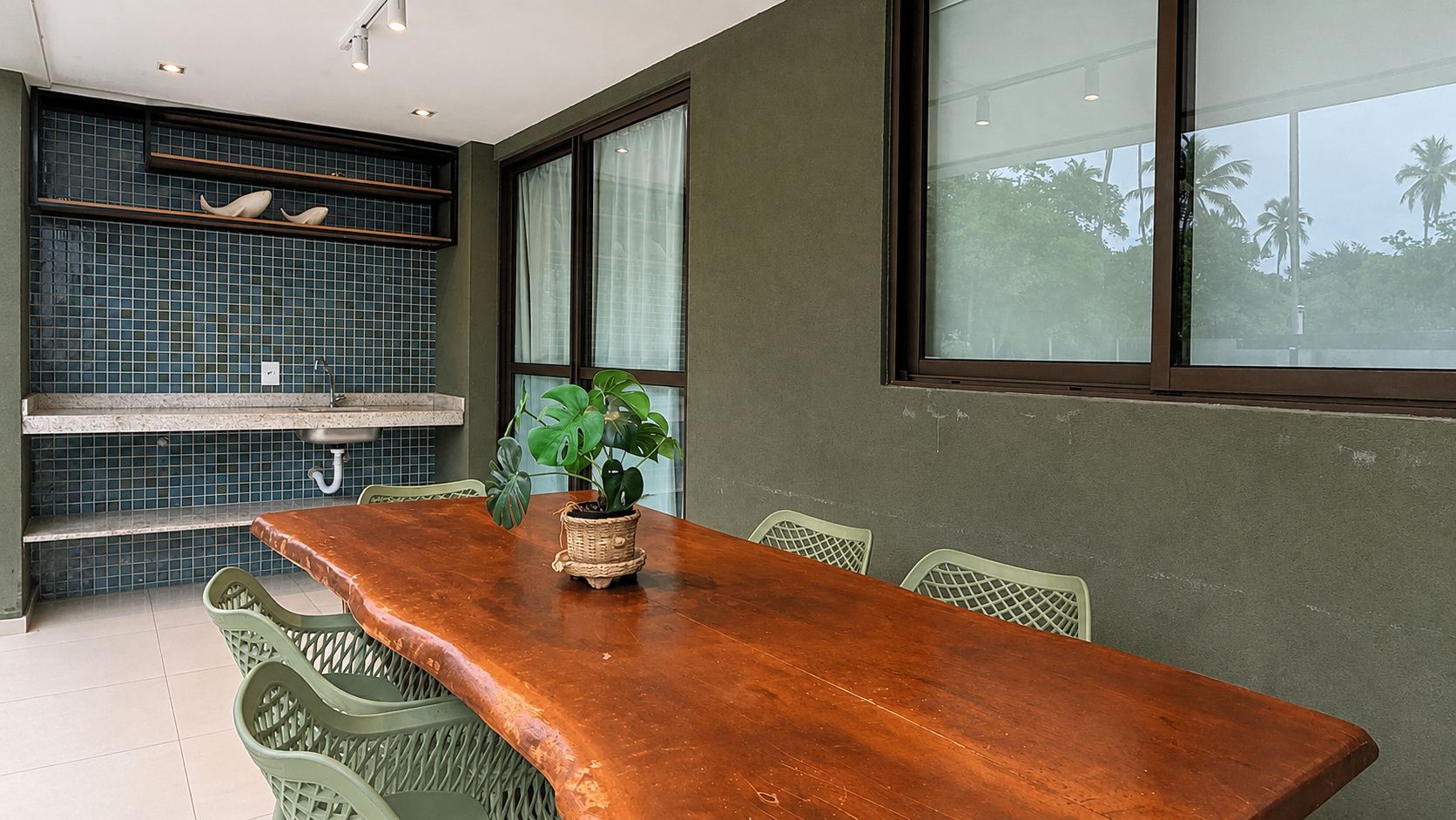 Uma sala de jantar com uma mesa de madeira, cadeiras verdes, uma planta em vaso e um revestimento de azulejos.