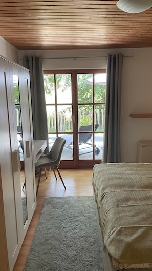 Un dormitori amb llit, escriptori i vista cap a l'exterior a través d'una porta corredissa de vidre.