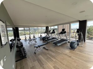 A gym with various exercise equipment, large windows, and a view of the outdoors.