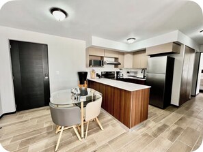 A modern kitchen with a central island, a dining area with a glass table, and a black door.