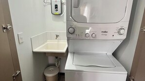 Een kleine wasruimte met een voorlader wasmachine, een wastafel en een toilet.