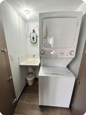 Une petite buanderie équipée d’un lave-linge à chargement frontal, d’un évier et de toilettes.