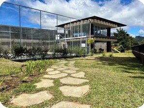 A modern building with a glass facade, a stone pathway leading to the entrance, and a fenced area with greenery.