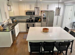 A modern kitchen with white cabinetry, stainless steel appliances, and a central island with chairs. - Delightful 2-bedroom house with AC in Sioux Falls (Sioux Falls)