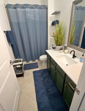 A bathroom with a shower curtain, toilet, sink, and a small step stool. - Delightful 2-bedroom house with AC in Sioux Falls (Sioux Falls)