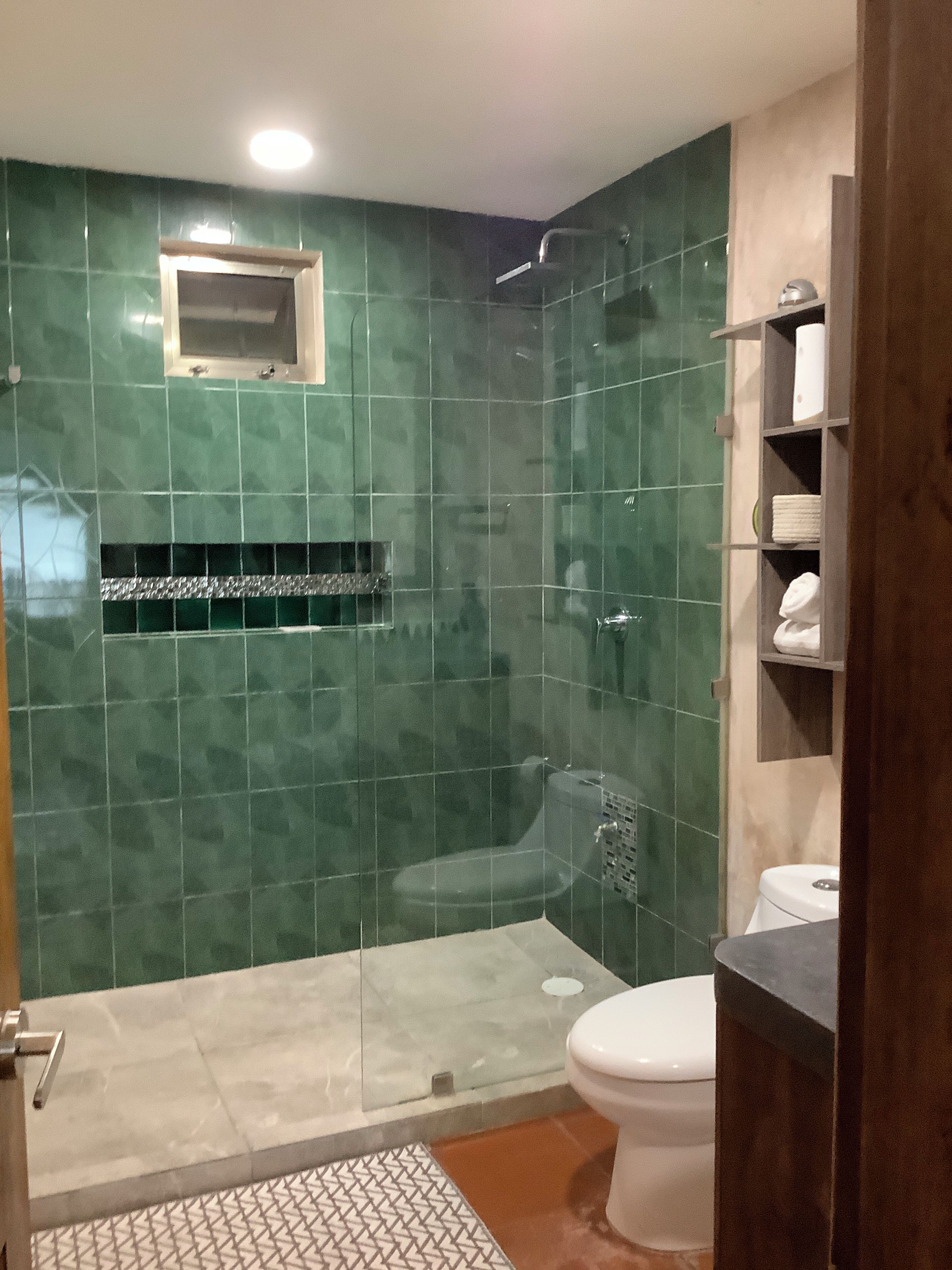 Un baño con ducha, inodoro y un estante con toallas.