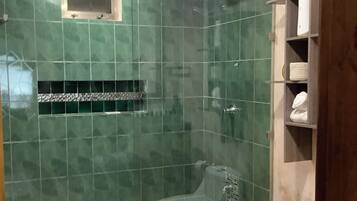 Un baño con ducha, inodoro y un estante con toallas.