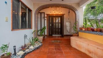 A hallway with a tiled floor, a door with glass panels, and potted plants.