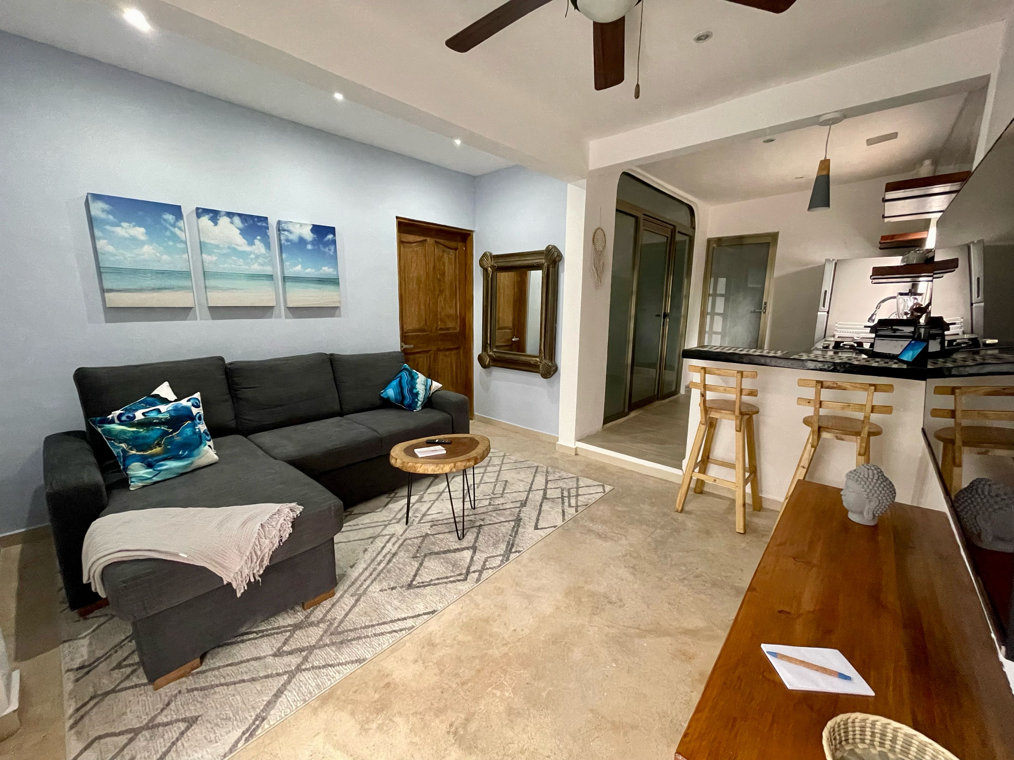 A modern living room with a sofa, a coffee table, and a dining area with a kitchen in the background.