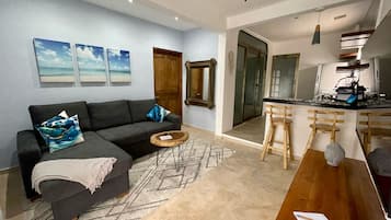 A modern living room with a sofa, a coffee table, and a dining area with a kitchen in the background.
