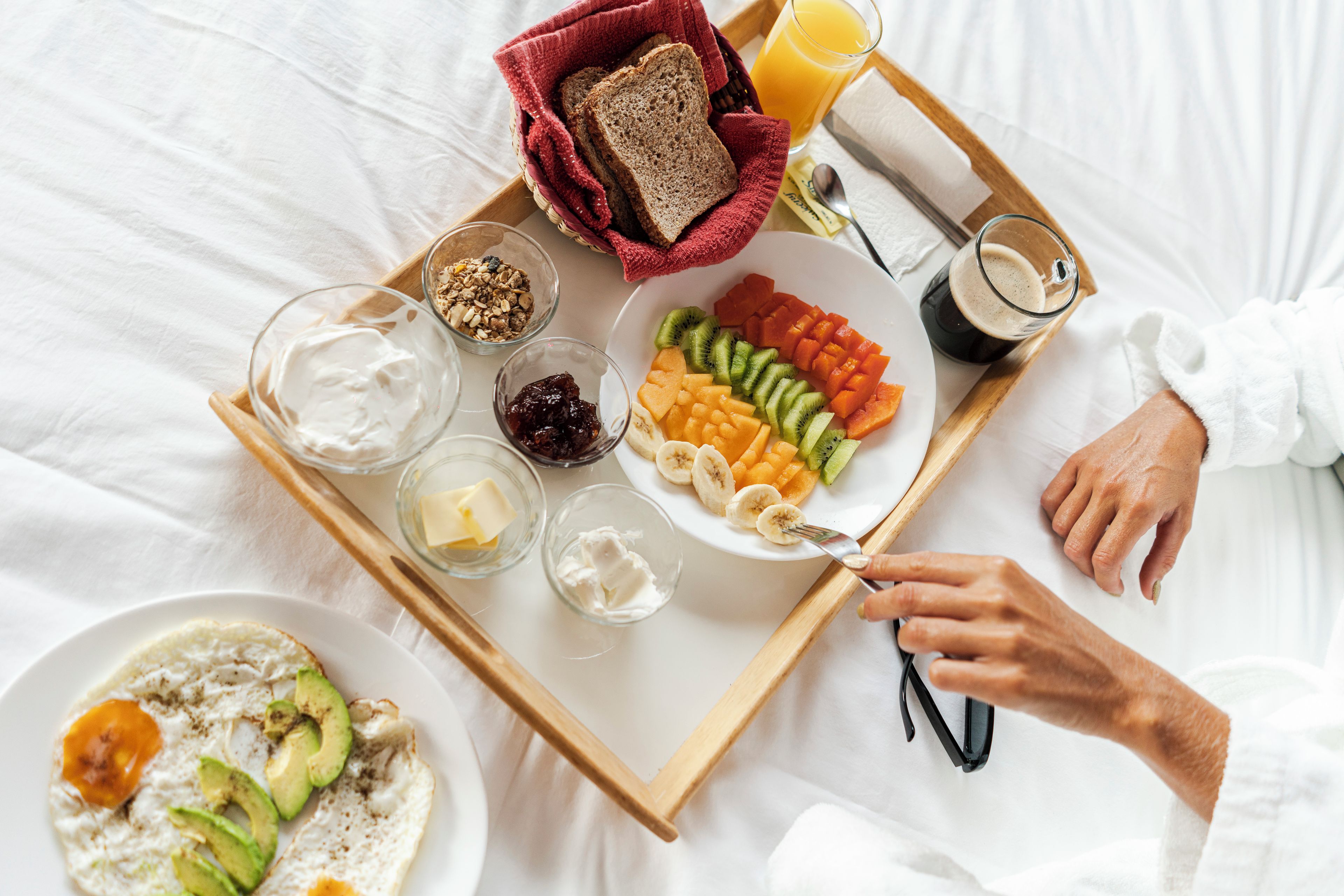 A breakfast tray with toast, fruit, yogurt, and juice on a bed.