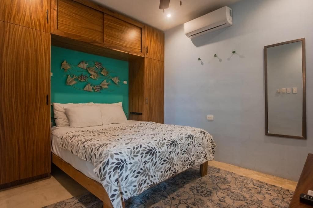 Un dormitorio con cama, armario de madera, aire acondicionado instalado en la pared y un espejo.