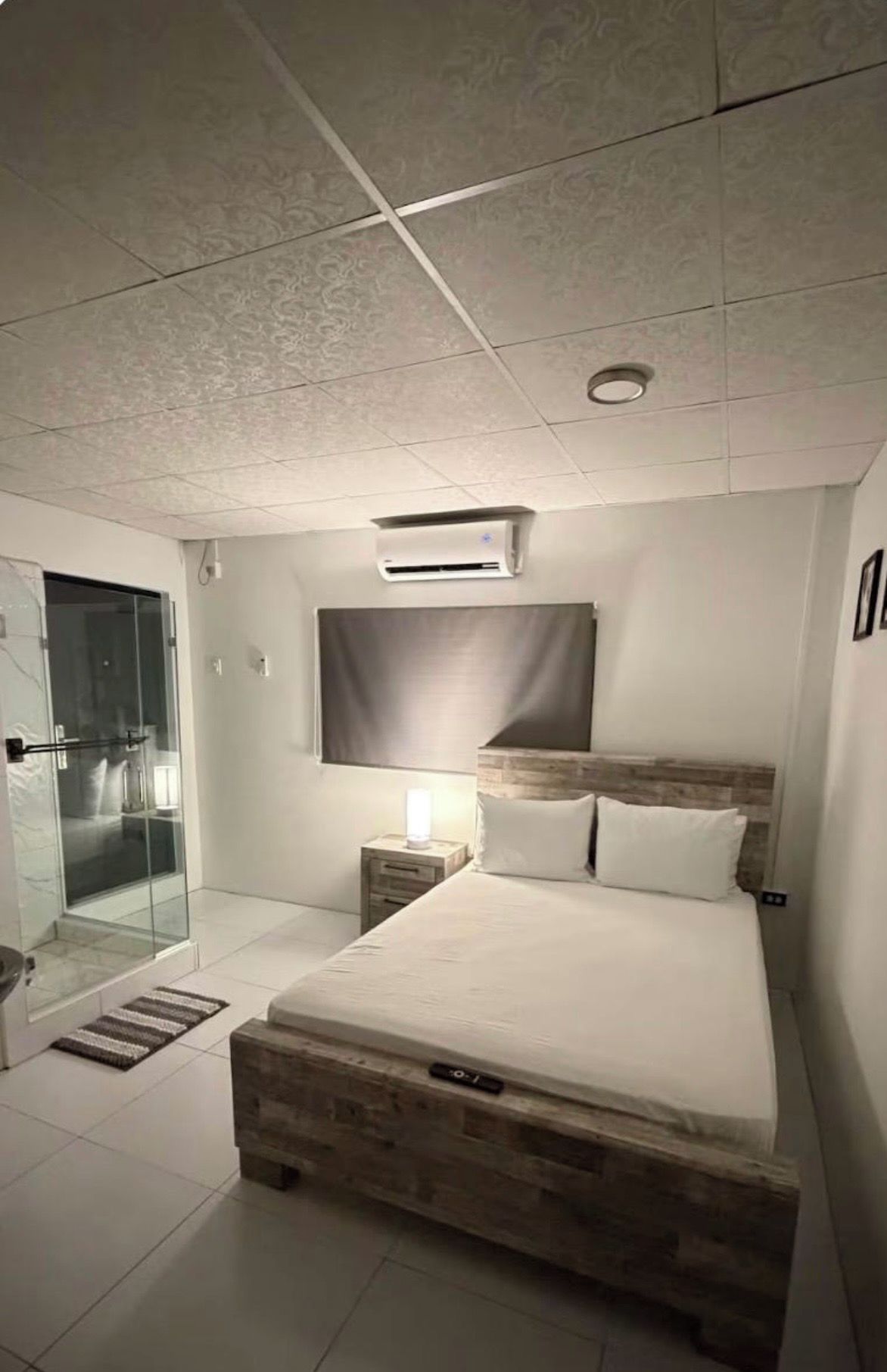 Ein modernes Schlafzimmer mit einem großen Bett, einer Duschkabine aus Glas und einer wandmontierten Klimaanlage.