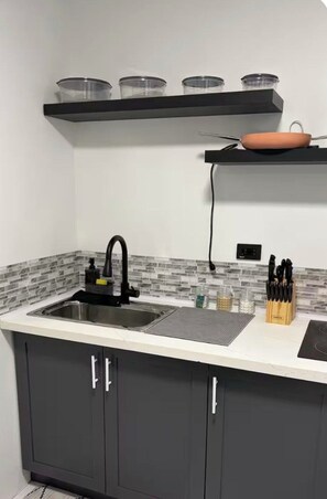 Eine moderne Küche mit einer schwarzen Arbeitsplatte, einem Edelstahl-Spülbecken und einem schwarzen Wasserhahn. Über der Arbeitsplatte befinden sich vier Gläser in einer schwarzen Vitrine.
