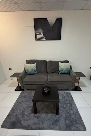 Un salon moderne avec un canapé gris, deux tables d’appoint, une table basse et un grand tableau abstrait accroché au mur.