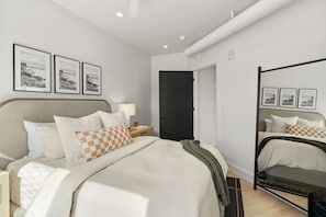 Une chambre à coucher moderne avec un lit, une table de chevet, une lampe et des tableaux encadrés accrochés au mur.