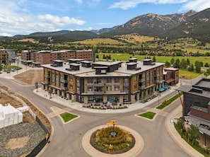 Un immeuble moderne à plusieurs étages, doté d’une cour intérieure, entouré d’un quartier résidentiel avec des maisons et ayant une chaîne de montagnes en toile de fond.