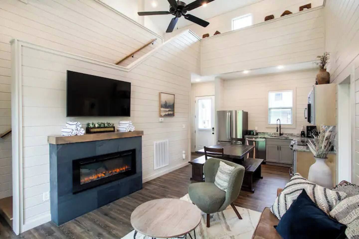 A spacious living room with a fireplace, a television mounted on the wall, and a ceiling fan.