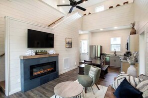 A spacious living room with a fireplace, a television mounted on the wall, and a ceiling fan. - Lake Access-Resort Beach-Modern-Games-Hot Tub (Sevierville)