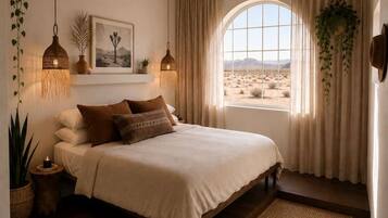 A bedroom with a large bed, a view of the desert through a window, and hanging plants.