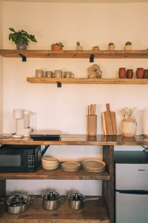 A kitchen with wooden shelves holding mugs, a coffee maker, a cutting board, and a Galanz refrigerator.