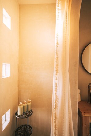 A bathroom with a shower curtain, a wooden bench, and three bottles of toiletries on a small round table.