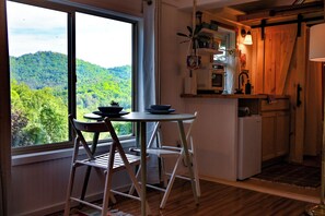 Eine Küche mit Blick auf einen bewaldeten Hügel, einem Esstisch mit Stühlen und einem Kühlschrank.