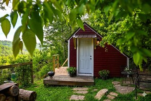 Eine rote Holzhütte mit weißer Tür, umgeben von viel Grün und einem Steinpfad.