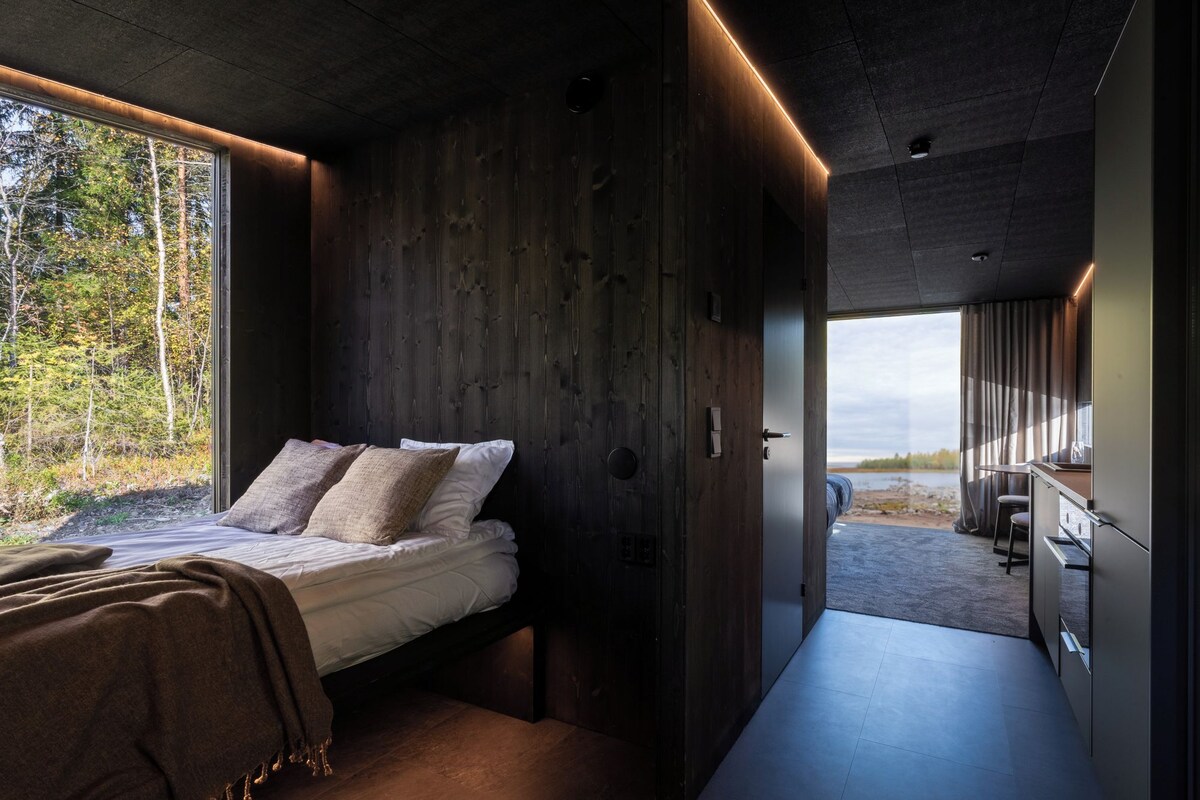 A modern interior with a bed, wooden walls, and a view of the outdoors.