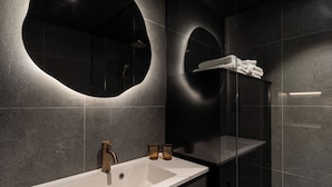 Un baño moderno con un lavamanos grande, un espejo y una ducha con mampara de vidrio.