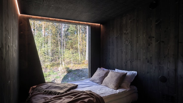 Un dormitorio con una cama, un ventanal y vistas a un bosque.