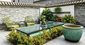 Una mesa de vidrio con sillas y una planta grande en un patio con paredes de ladrillo y plantas en macetas.