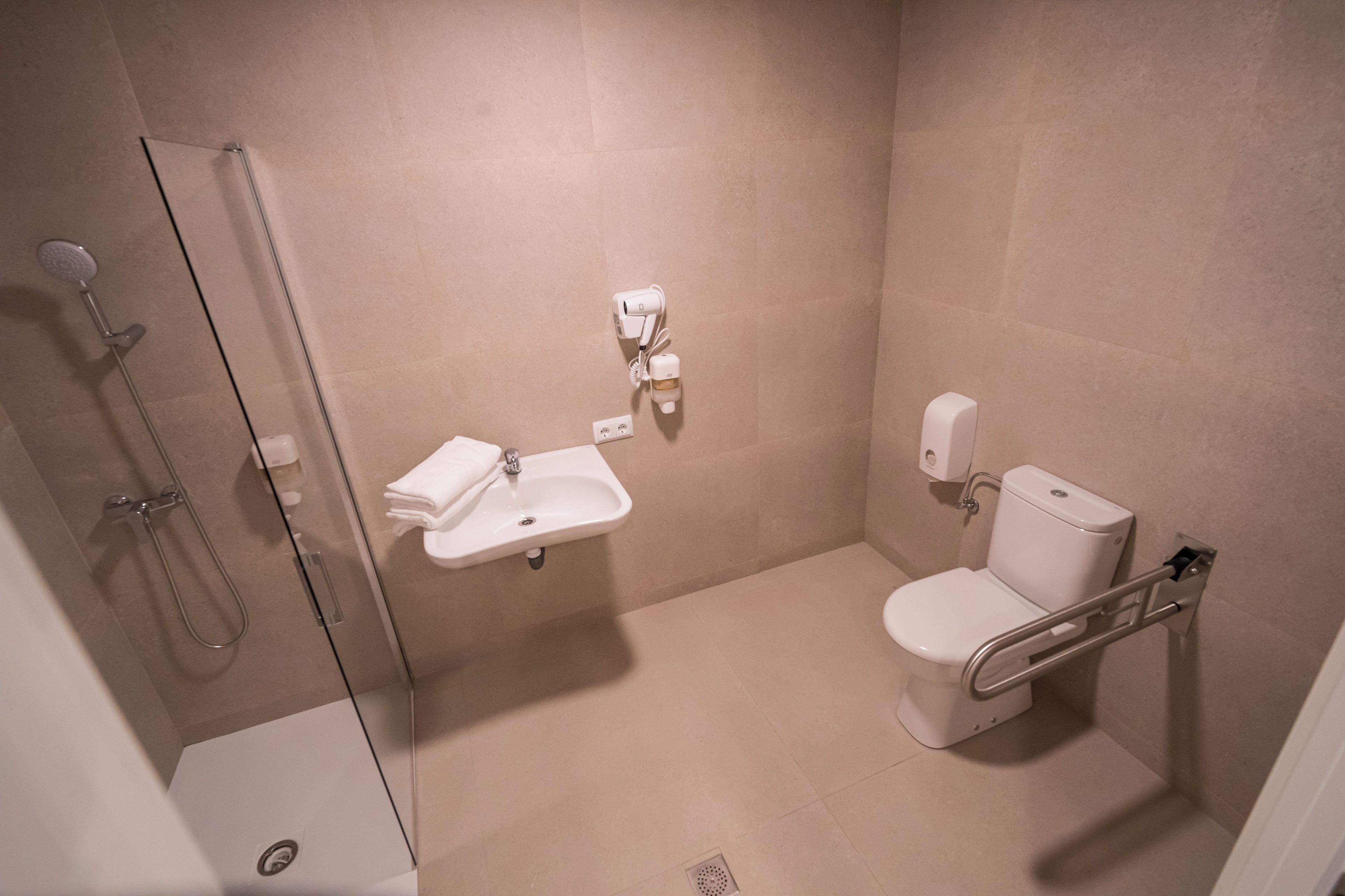 A bathroom with a glass shower enclosure, a sink, a toilet, and a hand dryer.