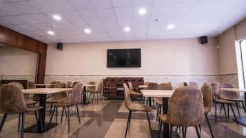 Un salón de conferencias con varias mesas y sillas, un televisor de pantalla plana montado en la pared y un mueble de madera con estantes.