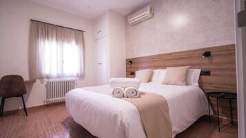 Een hotelkamer met een groot bed, een houten hoofdbord, een radiator, een stoel, een klein tafeltje en een raam met gordijnen.