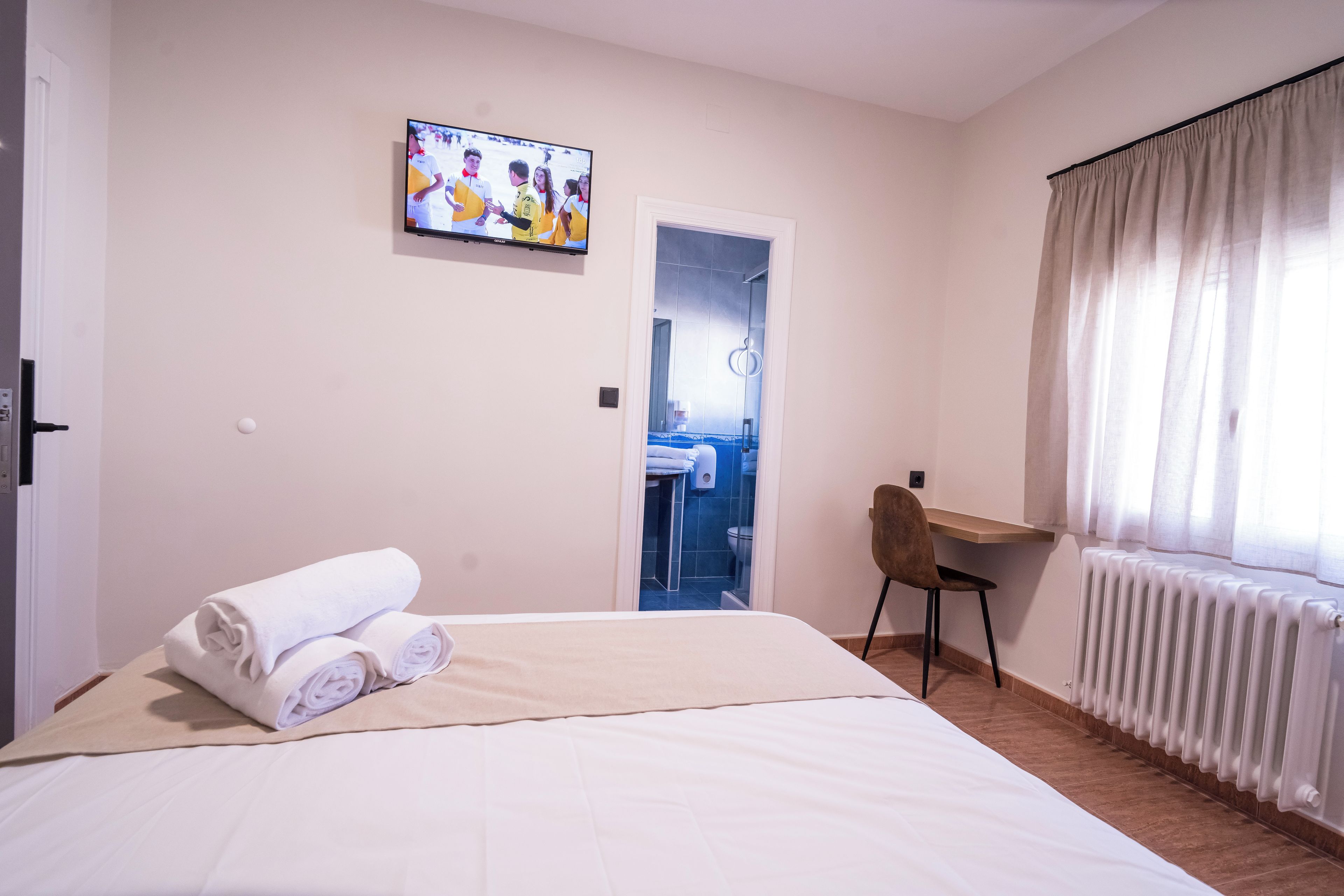 Habitación de hotel con cama, escritorio, silla, televisión y baño visible a través de una puerta abierta.