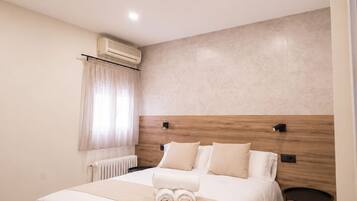 Una habitación de hotel moderna con una cama grande, una mesita de noche, un equipo de aire acondicionado y una ventana con cortinas.