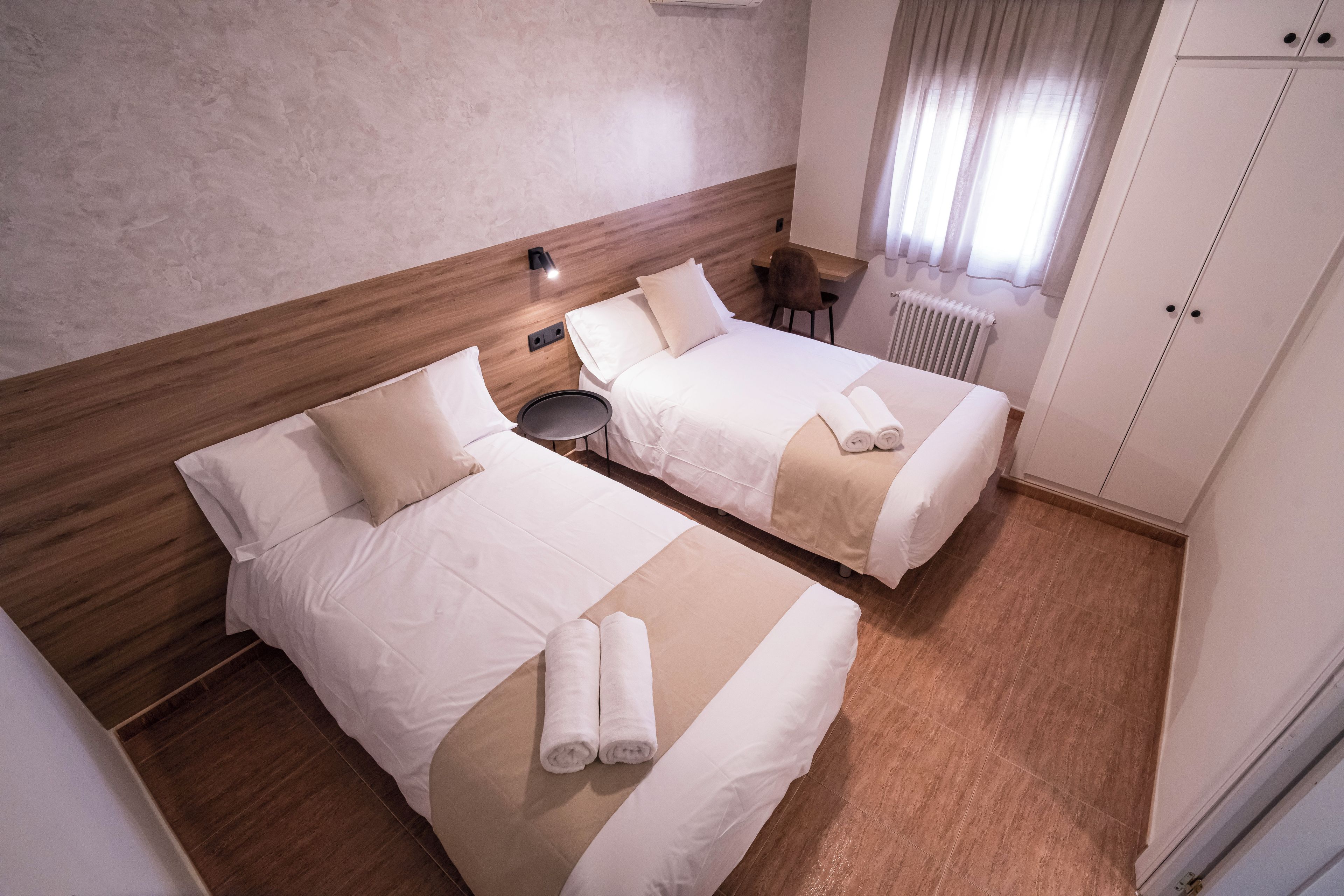 Una habitación de hotel con dos camas, una mesita redonda pequeña, una silla y un radiador.