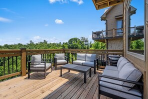 A wooden deck with outdoor furniture, a stone building with a balcony, and a view of greenery. - Lake View Cabin · Sleeps 16 · Hot Tub · Games (Sevierville)