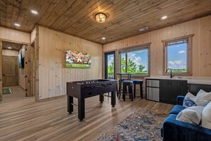 A wooden interior with a foosball table, a TV, and a kitchen area. - Lake View Cabin · Sleeps 16 · Hot Tub · Games (Sevierville)
