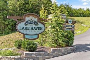 En välkomstskylt för Lake Haven Cabins Resort, med en illustration av ett berg och en stuga, en pil som visar riktningen och en skylt med texten "Snart öppnar vi".