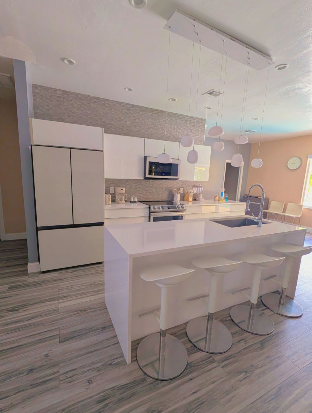 A modern kitchen with a central island, bar stools, and a microwave.
