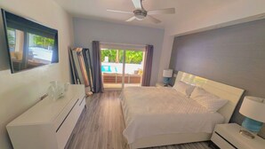 Ein Schlafzimmer mit Bett, Nachttischen, Deckenventilator, großem Fenster und Blick auf einen Außenpool.