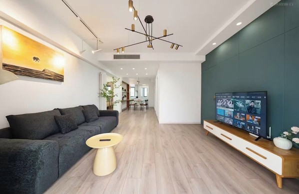A modern living room with a sofa, a coffee table, a TV on a wooden stand, and a wall-mounted artwork.