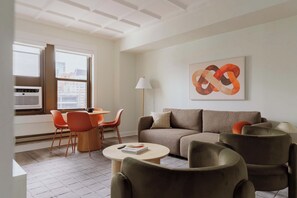 Een moderne woonkamer met een bank, fauteuils, een salontafel en een groot abstract schilderij aan de muur.