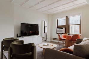 A modern living room with a flat-screen TV, comfortable seating, a dining area with a table and chairs, and large windows offering a city view. - Luxury Designer Apartment 1003|Gold Coast/Old Town (Chicago)