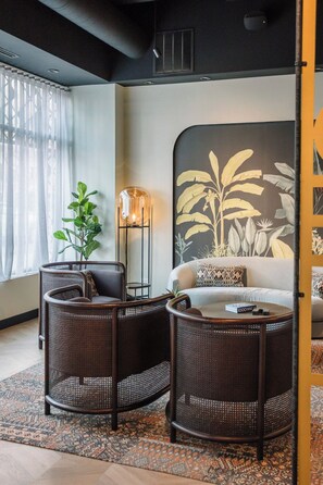Ein modernes Wohnzimmer mit einer Couch, zwei Korbstühlen, einer Stehlampe und einem großen Wandbild.