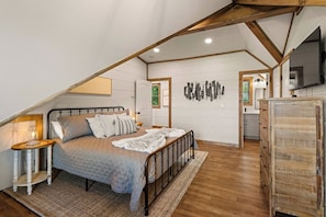 Ein Schlafzimmer mit geneigter Decke, einem Bett mit Kopfteil, einem Nachttisch mit Lampe und einer Kommode.