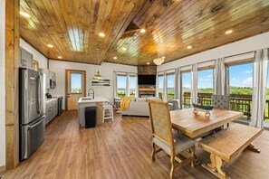 Eine moderne Küche mit integrierter Kochinsel, einem Essbereich mit Holztisch und -stühlen sowie großen Fenstern mit Blick ins Freie.